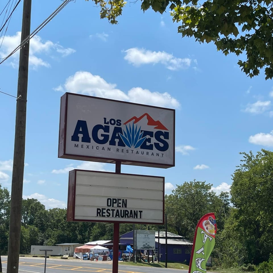 Los Agaves Mexican Restaurant sign with "OPEN RESTAURANT" below, against a blue sky.