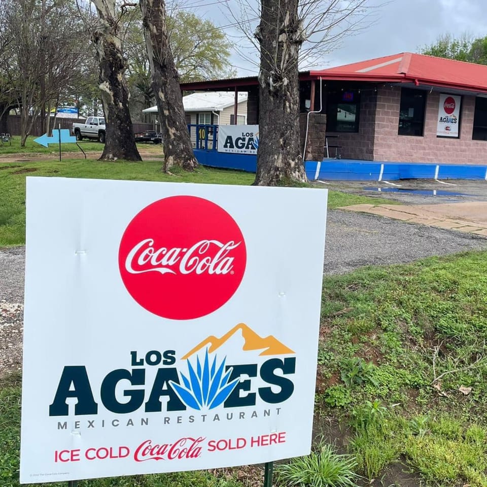 A Los Agaves Mexican Restaurant sign with Coca-Cola branding in front of the restaurant building.