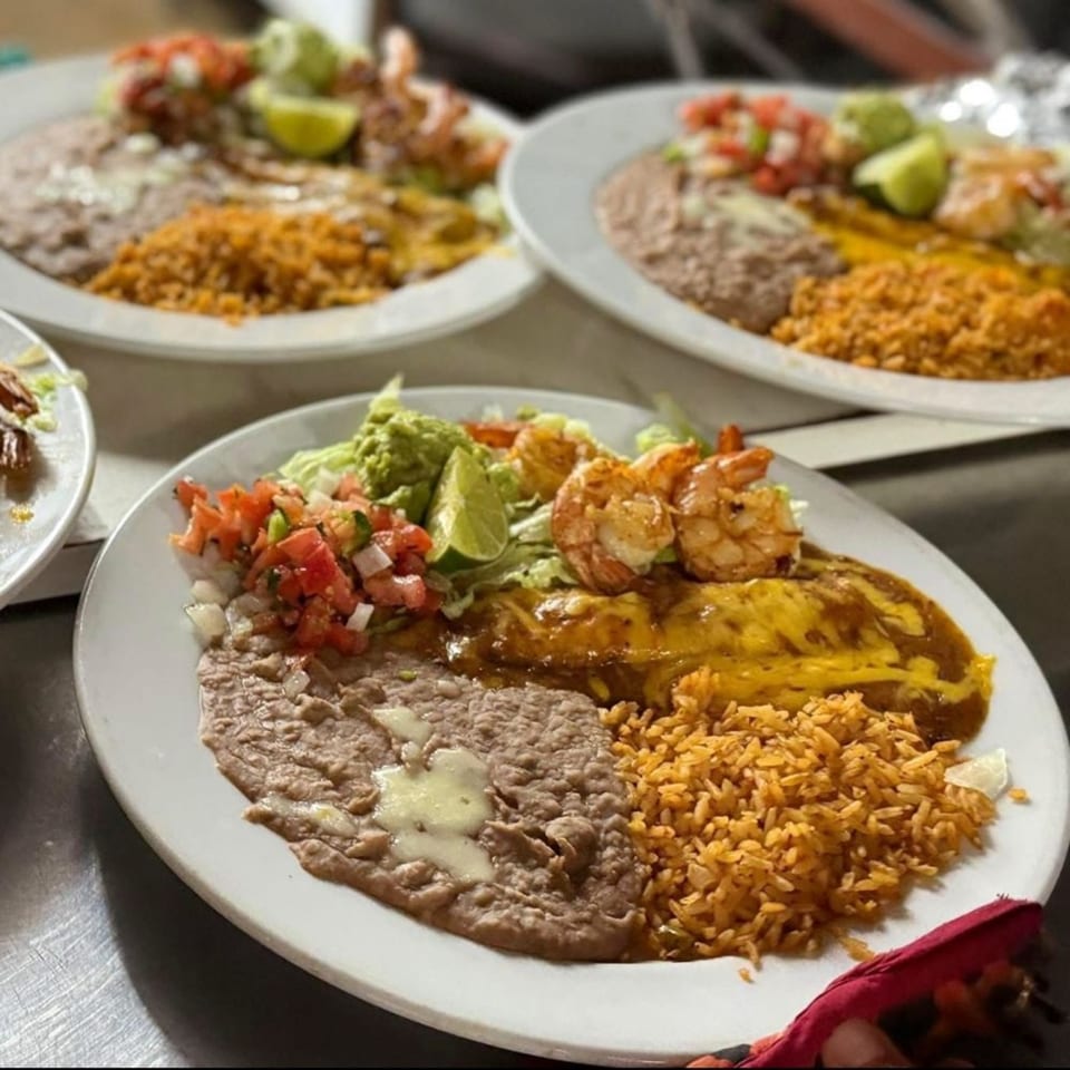 Three plates of Mexican food with shrimp, enchiladas, rice, beans, guacamole, and pico de gallo.
