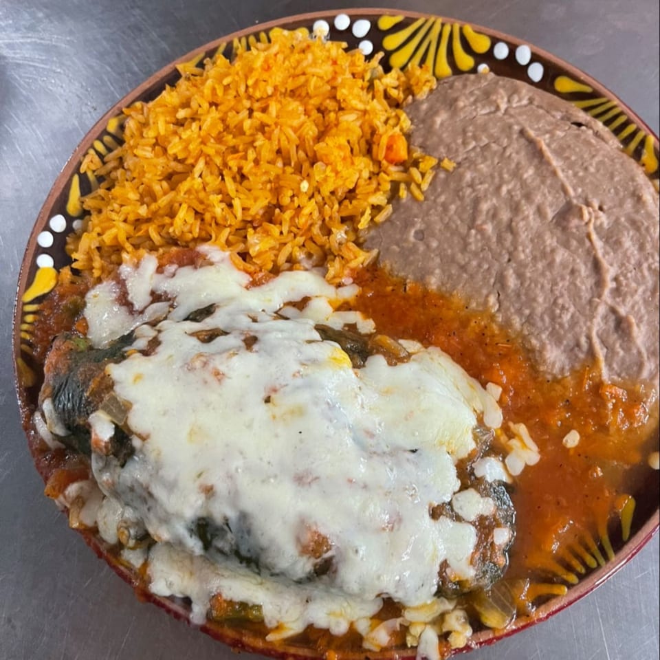 A Mexican dish with a cheese-covered chile relleno, orange rice, and refried beans on a decorative plate.