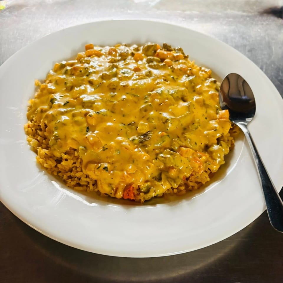Mexican rice dish topped with a creamy yellow sauce, vegetables, and a spoon on a white plate.